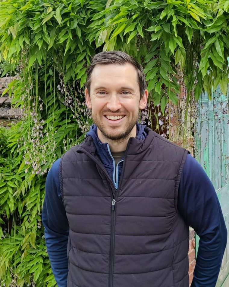 Dr Daniel O'Rourke, clinical psychologist, smiling in front of climbing wisteria